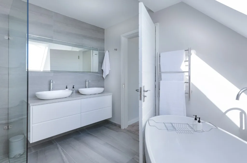White bathroom with round mirror, tub shower, and modern vanity